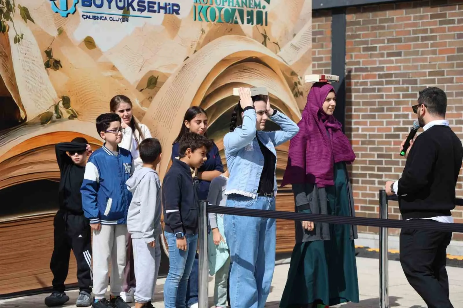 KOCAELİ KİTAP FUARI’NDA ZİYARETÇİLER, “BAŞIMIN ÜSTÜNDE YERİN VAR” OYUNUNDA KİTAPLARI BAŞLARININ ÜZERİNDE DÜŞÜRMEDEN TAŞIMAK İÇİN YARIŞTI. DENGE VE DİKKAT GEREKTİREN OYUN, FUAR ALANINDA RENKLİ VE EĞLENCELİ GÖRÜNTÜLERE SAHNE OLDU.